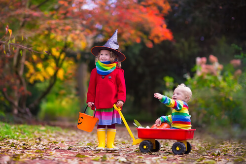 Little girl in a Halloween costume with little boy in a wagon